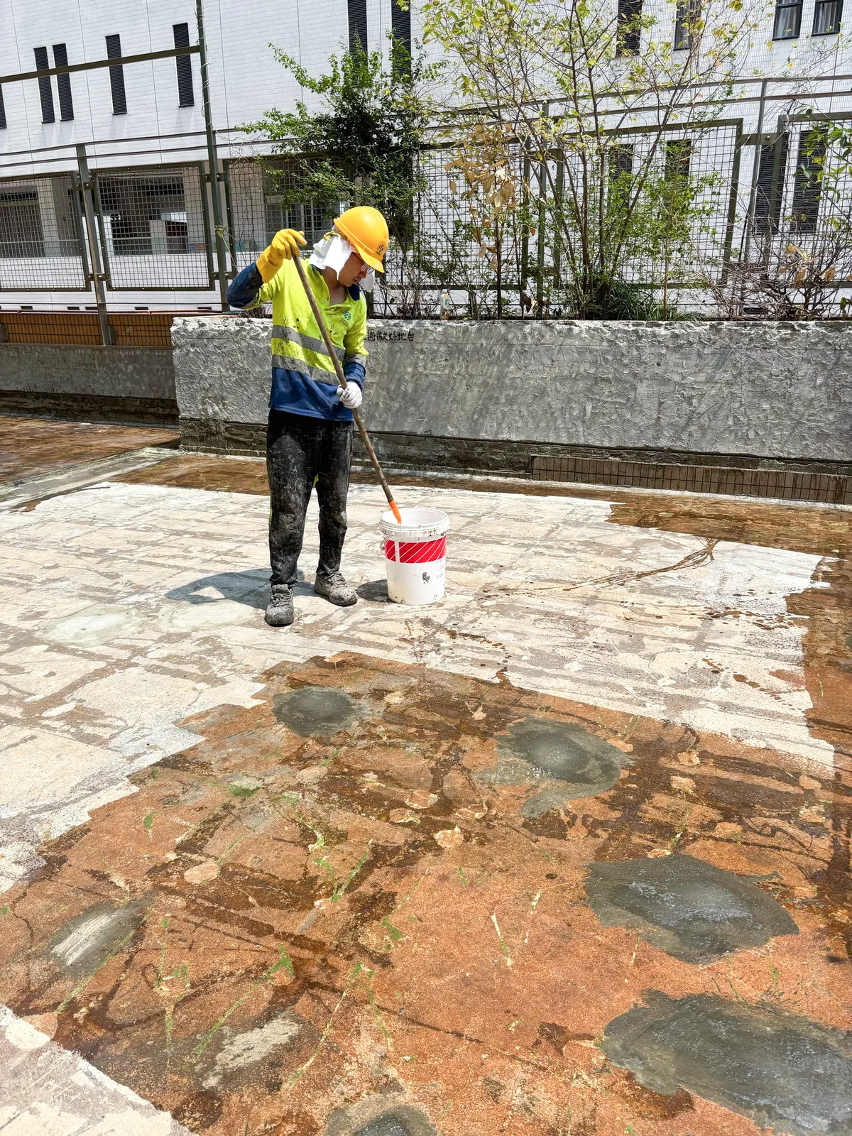 香港浸會大學天台上,工人在多個灰色地面處理位置旁攪拌施工用料