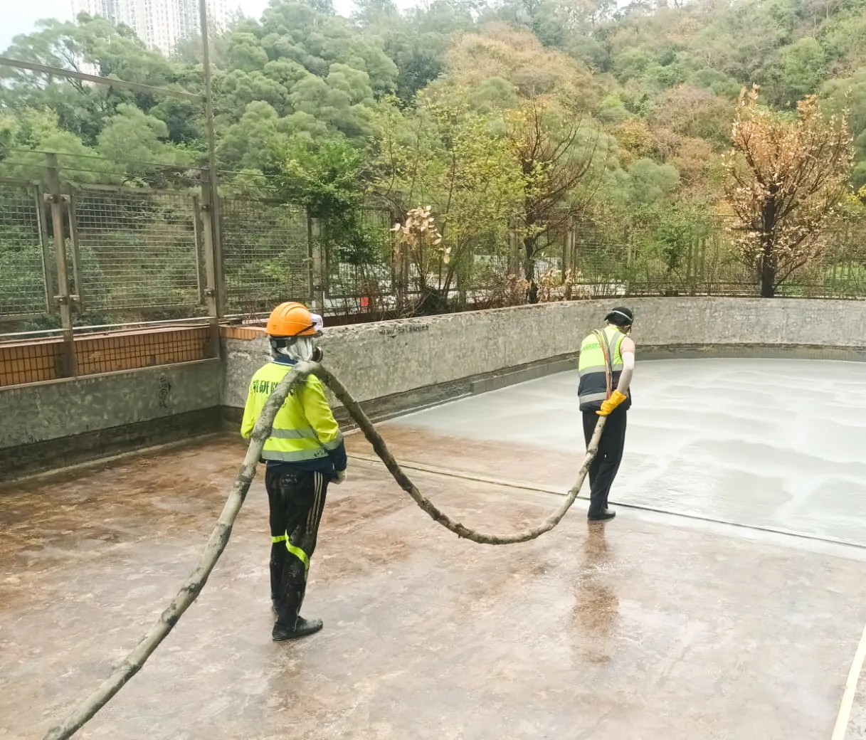 香港浸會大學天台上,兩名工人以輸料管及長柄工具處理大面地台