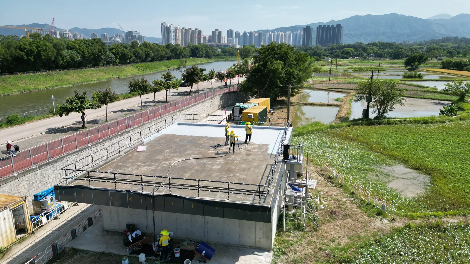 古洞機房天台的高角度視圖,工人身後可見道路、田野及遠處住宅樓宇