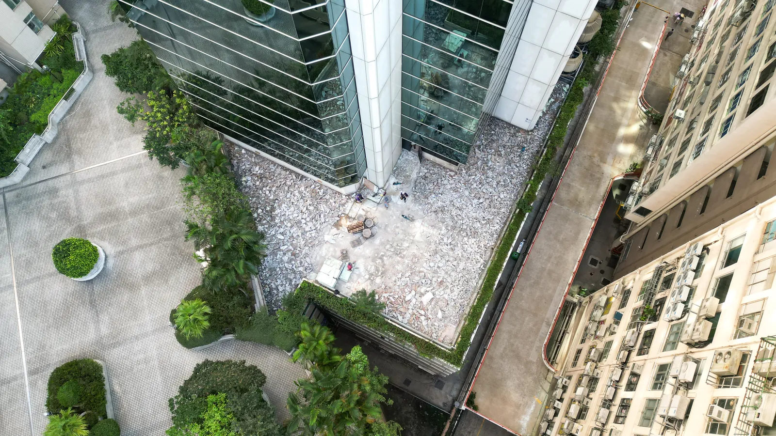 高處俯瞰炮台山理文商業中心玻璃大樓旁的平台,可見淺色碎塊及數名工人