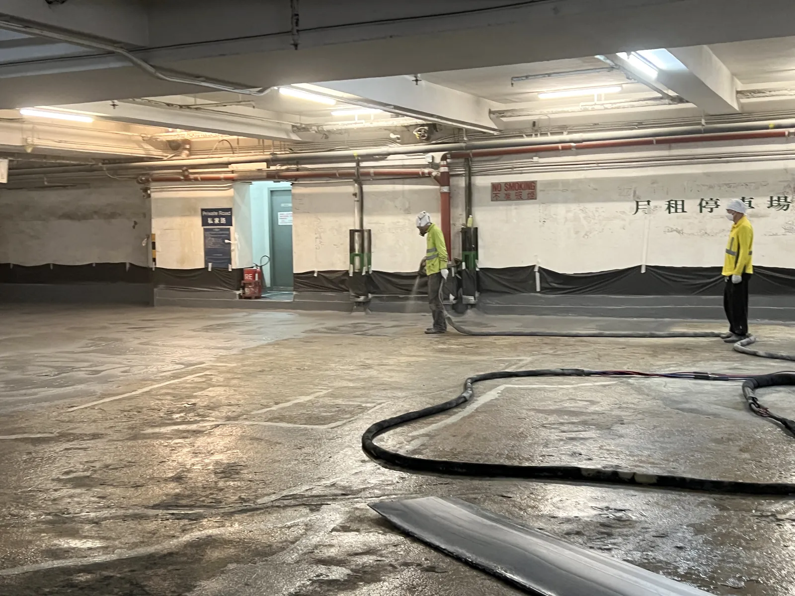 炮台山理文商業中心停車場內兩名工人在濕潤地面操作粗黑色軟管