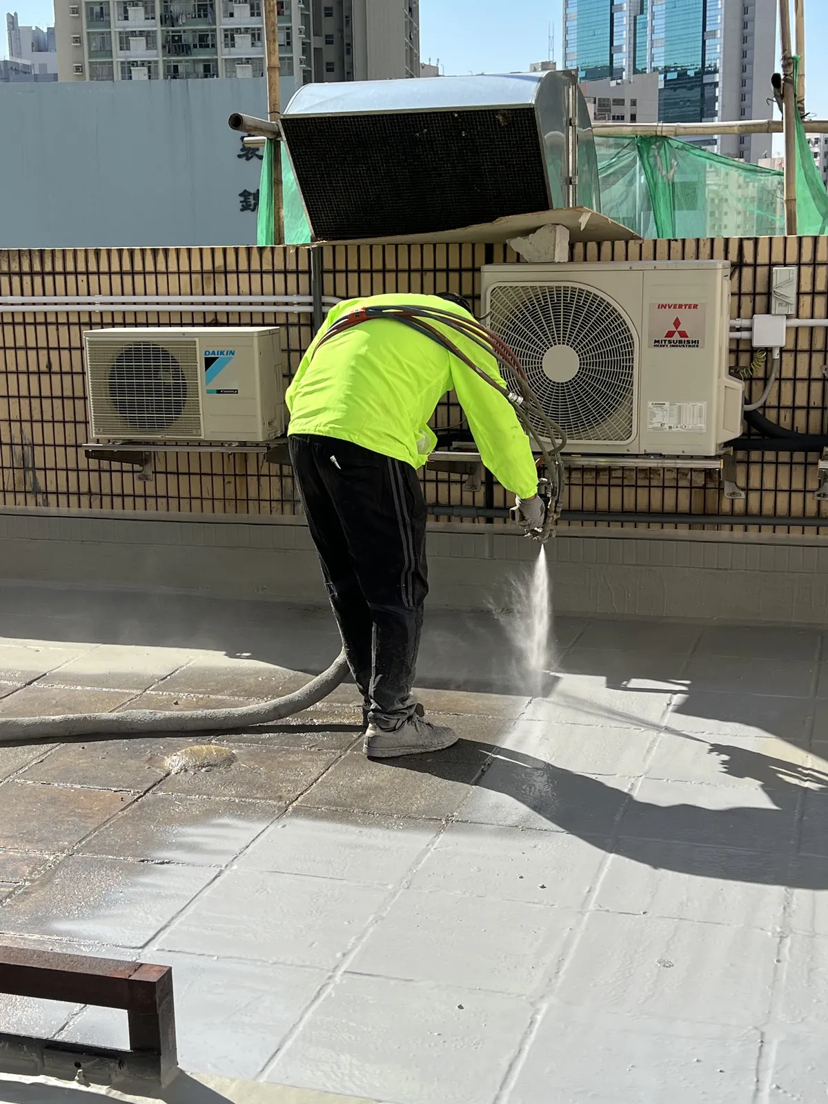 葵涌安蔭商場工人在冷氣機下方以輸料管噴灑灰色天台地面