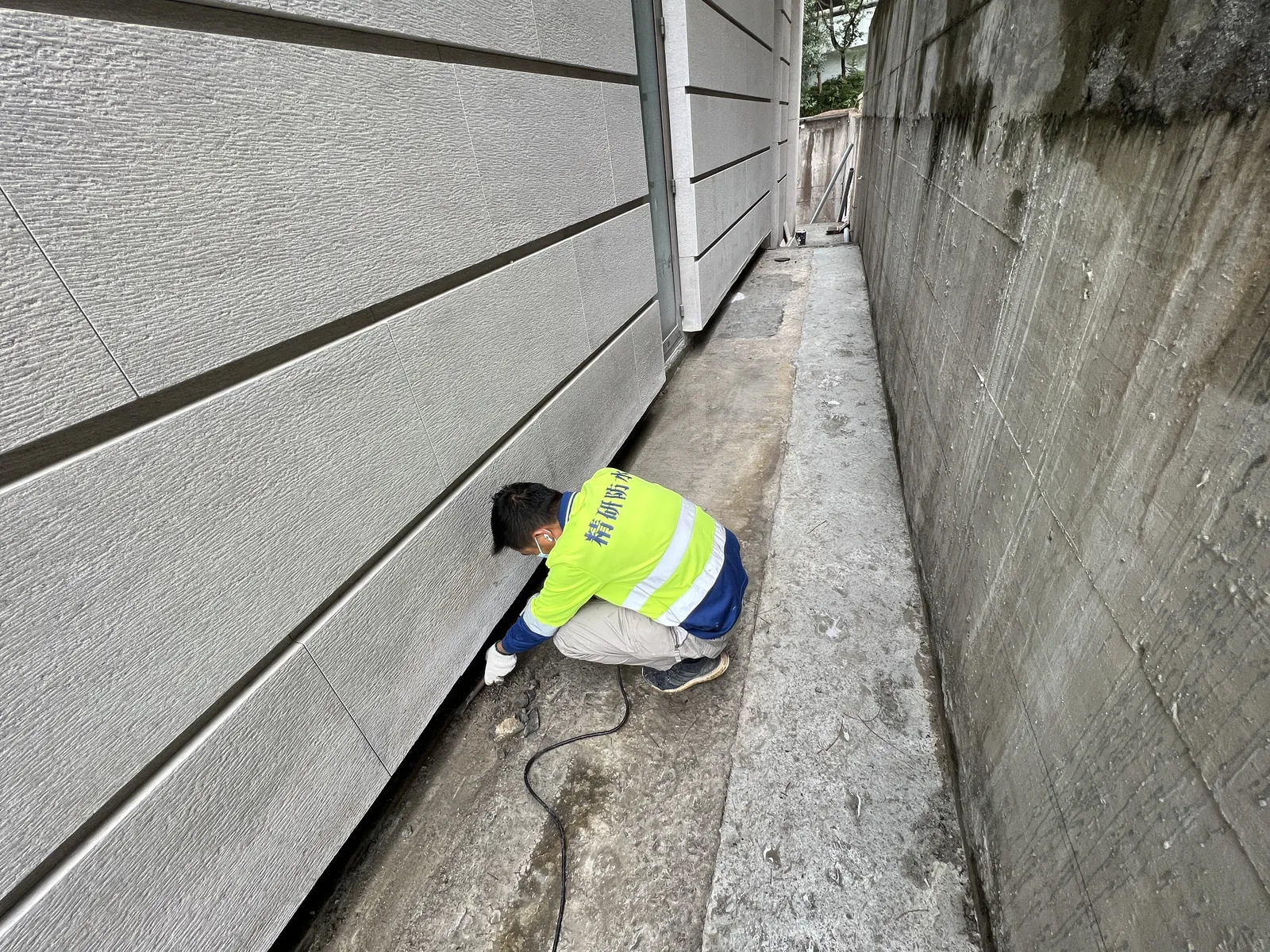 淺水灣藍灣道住宅外牆與混凝土牆之間,工人蹲在狹窄通道處理地面邊位