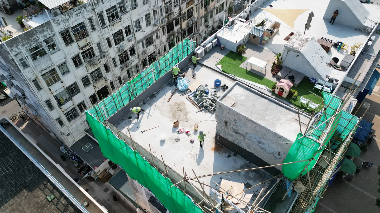 西貢灣景街天台航拍，屋面四周搭有綠網棚架並有多名工人和設備