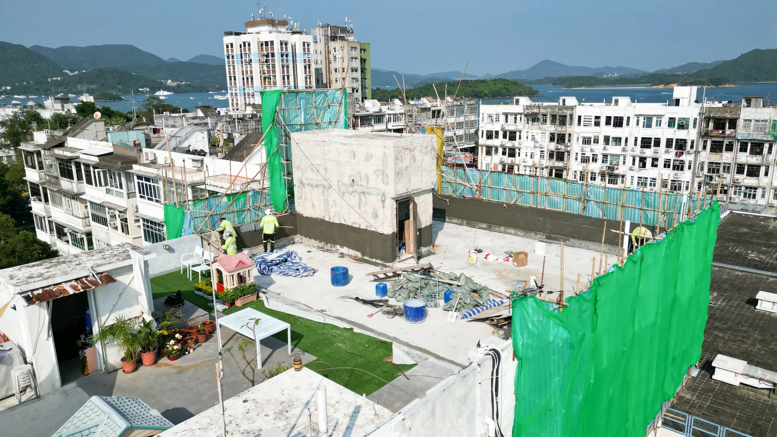 西貢灣景街天台工程全景，可見綠網棚架、工人、桶具及遠處山海景