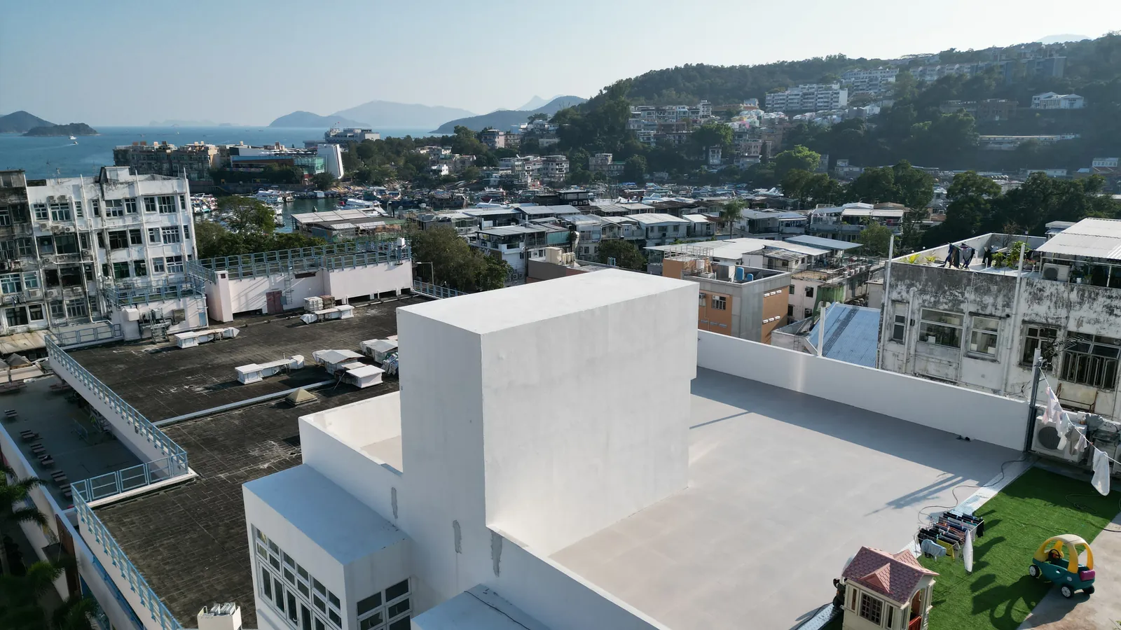 西貢灣景街白色天台斜角航拍，背景可見西貢樓宇、山坡及海岸